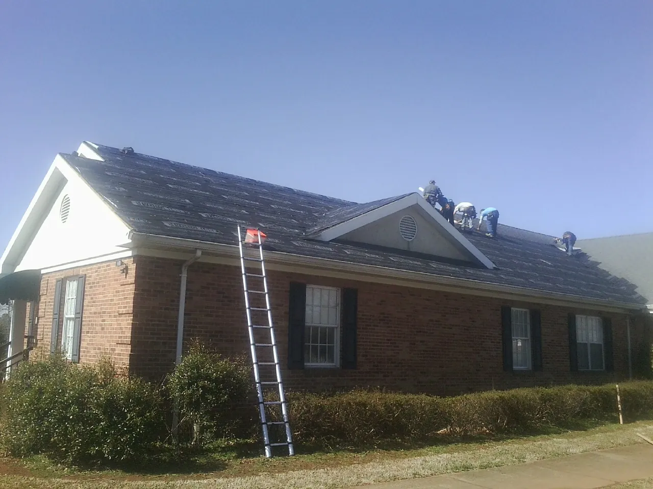 Crew tearing shingles off a brick ranch roof with a ladder set — Emergency Roof Repair work by our crew in Maumee