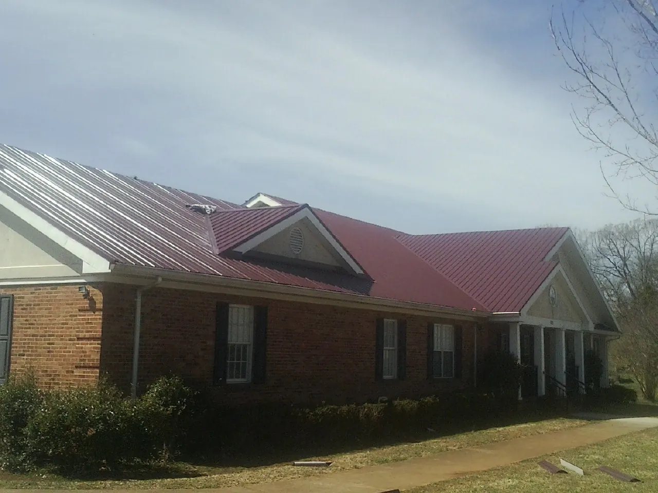 Red metal roof with gabled entries on a long brick building, from a Hail Damage Roof Repair job in Maumee