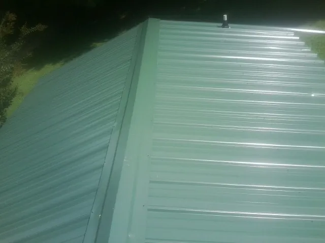 New green metal panels meeting at the ridge of a roof — Flat Roof Repair work by our crew in Maumee