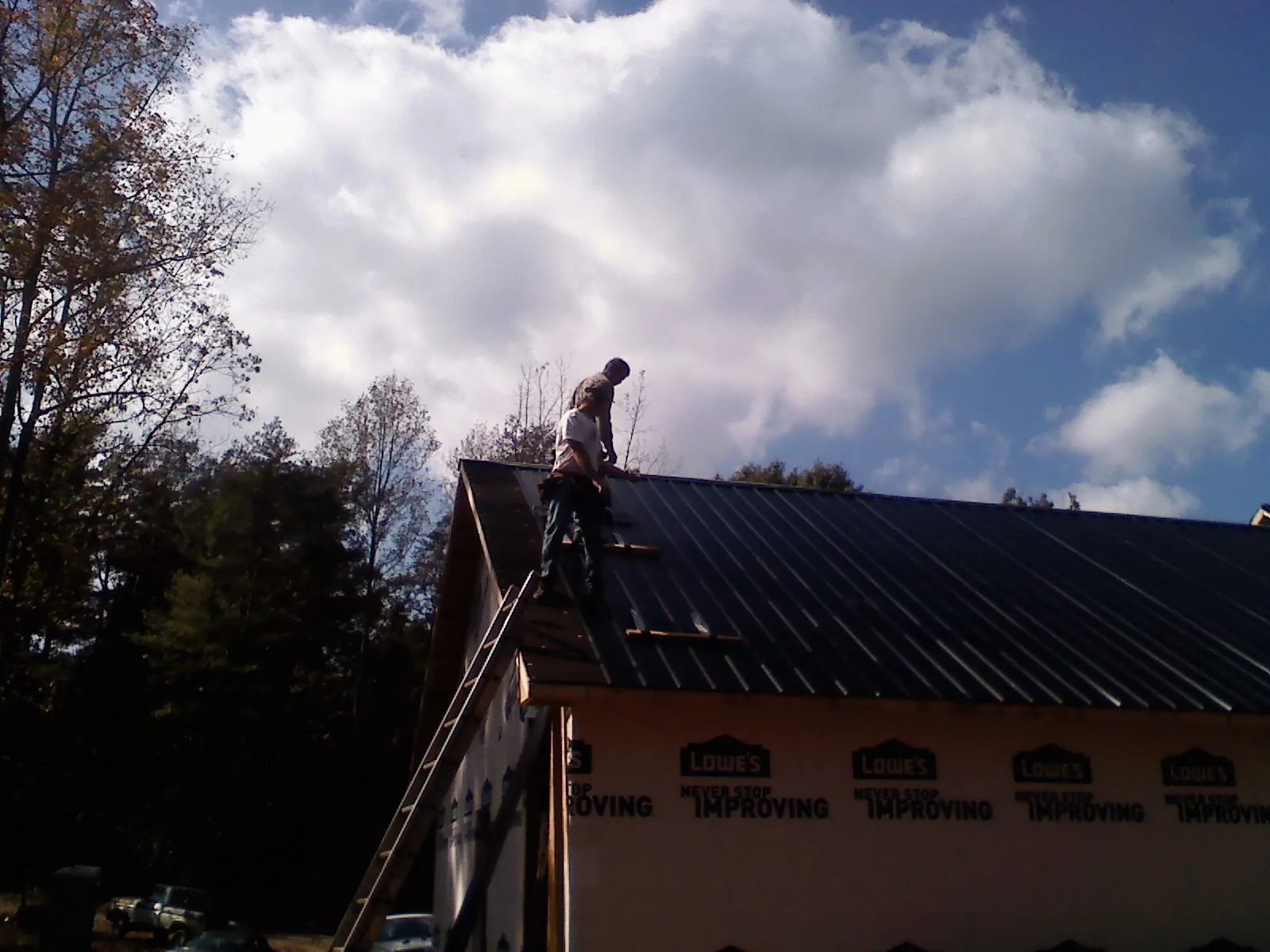 Roofer fastening dark metal panels high against a cloudy sky, from a Roof Inspection job in Maumee