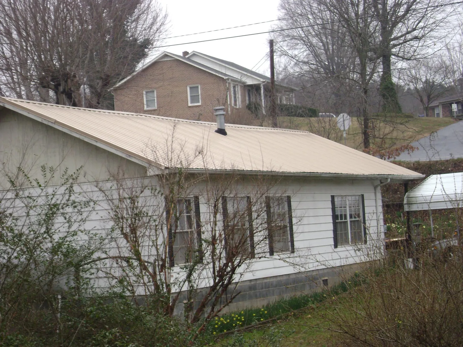 Tan metal roof on a white sided house set into a hillside — Commercial Roofing by Roofing Brothers in Maumee